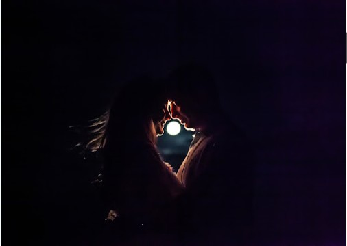 Silhueta de um casal frente a frente na escuridão, iluminado apenas pela lua cheia entre os dois.